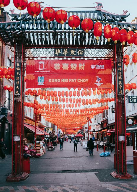 This image captures a busy street scene at Piccadilly Circus in Chinatown, WC2, with a prominent traditional Chinese-style archway featuring intricate blue, gold, and red decorative elements and a til